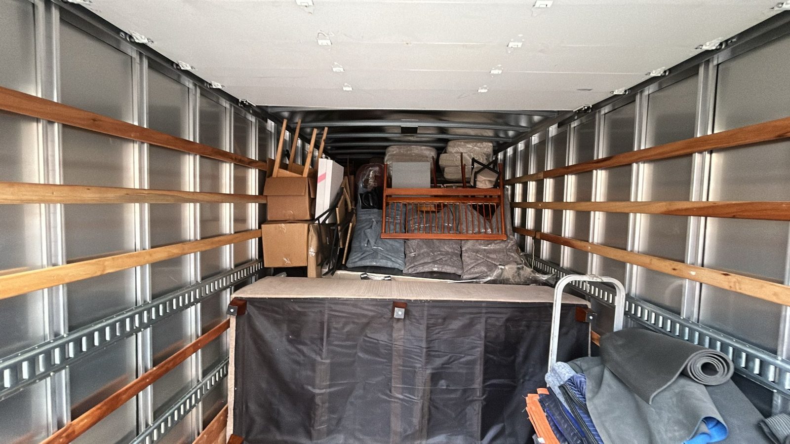 Inside a Homeboy Movers truck loaded with wrapped furniture, boxes and a dolly