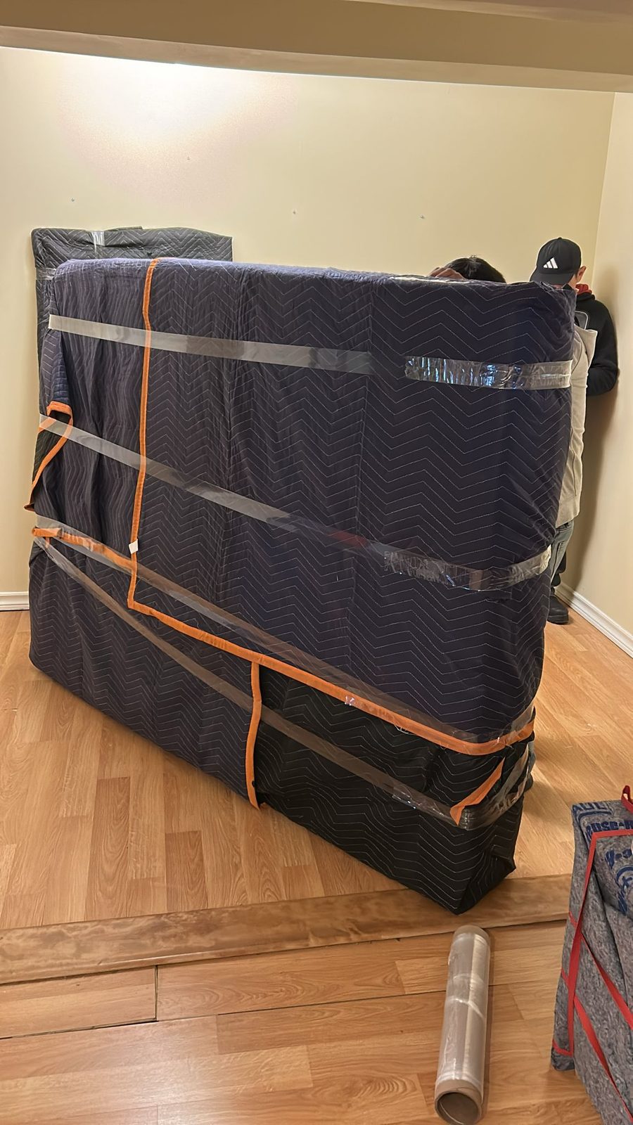 A large piece of furniture wrapped in a moving blanket and strapped, with a Homeboy Movers crew member alongside
