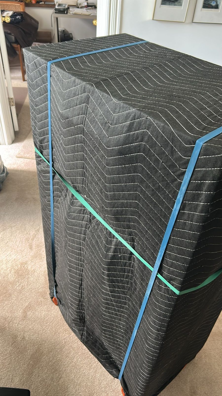 A tall item fully covered in a padded moving blanket and secured with straps