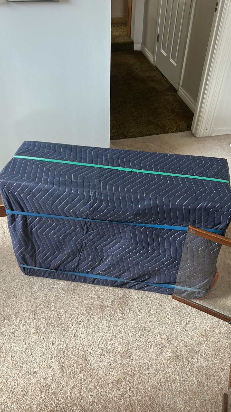 A piece of furniture wrapped in a padded moving blanket and strapped, ready to carry out